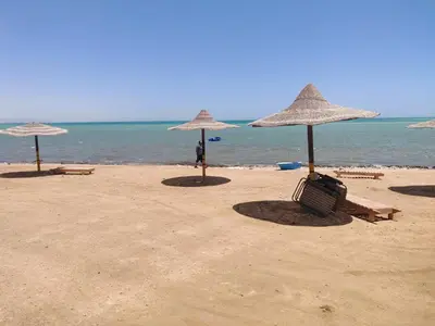 three umbrellas and chairs on a beach with the ocean at 2bedroom apartment in Summer Land Beach Resort in Hurghada