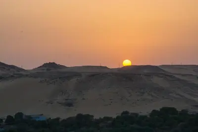 a sunset in the desert with the sun on the horizon at ASWAN NILE PALACE (swimming pool-rooftop-Nile view) in Aswan