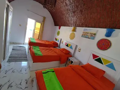 two beds in a bedroom with orange and green sheets at Lawanda Nubian B&B in Aswan
