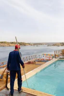 a man standing next to a swimming pool with a stick at Fenti Nubian Resort in Aswan