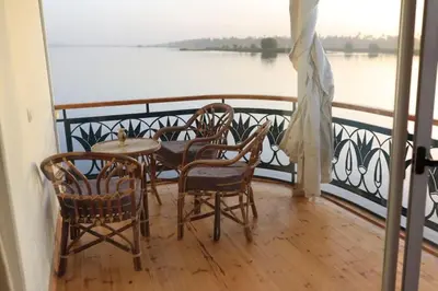 a table and chairs on a balcony with a view of the water at Embrace 1 Nile Sailing Dahabiya in Luxor