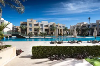 a resort with a swimming pool and palm trees at Jazzy 1BDR w Outdoor Pool View Terrace Free Pool & Beach Access in Hurghada