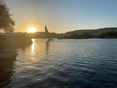 a sunset on a lake with a sailboat in the water at Houseboat Hotel and Nile Cruises Zainoba in Aswan