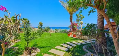 a garden with a lawn and trees and the ocean at Luxury Seafront Pool Villa - 3 Stories & Roof floor - All Master Bedrooms in Hurghada