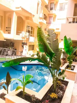 a swimming pool with plants in front of a building at Palma house apartments A8 in Hurghada