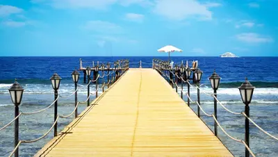 a wooden pier with an umbrella on the ocean at Bliss Nada Beach Resort in Coraya Bay