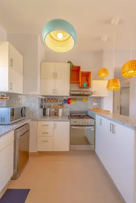 a kitchen with white cabinets and a blue light fixture at Sunny 2 Bedroom + Private Roof Terrace Lagoon View in Hurghada