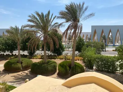 a garden with palm trees and a building in the background at Lovely two bedroom apartment in Hurghada