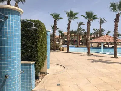 a blue tile wall next to a swimming pool with palm trees at Apartman Veranda in Hurghada