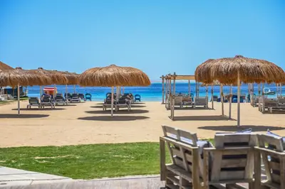 a beach with chairs and straw umbrellas and the ocean at AJIRA Bay Hotel Hurghada Marina in Hurghada