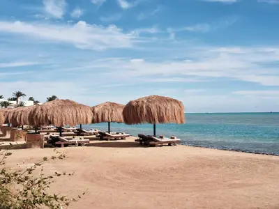 a beach with chairs and straw umbrellas and the ocean at Club Paradisio El Gouna Red Sea in Hurghada