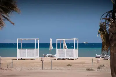 two umbrellas and chairs on a beach with the ocean at Lovely 1 Bedroom apt. At Mangroovy residence with free access to the Beach and Pools in Hurghada