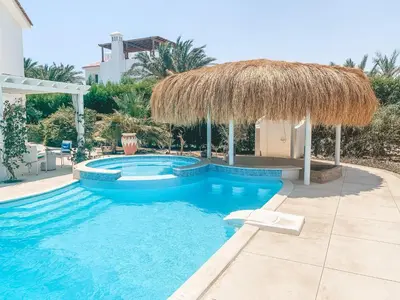 a swimming pool with a large straw umbrella and a swimming pool at Snow White Villa in Hurghada