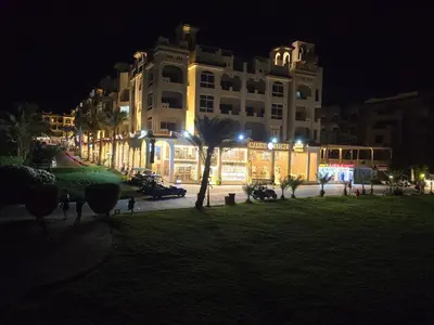 a large building at night with a palm tree in front at Sahl Hasheesh, El Andalous by All View apartements in Hurghada