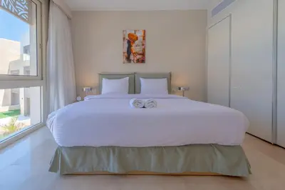 a bedroom with a large white bed with two towels on it at High Standard 2-Bedroom in Mangroovy Residence, Pool View & Beach in Hurghada