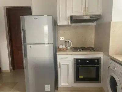 a white kitchen with a refrigerator and a stove at Sabina 1br apartment Lagoon view with shared pool By BFG Beit Fel Gouna in Hurghada