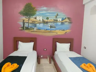 two beds in a room with a painting on the wall at Nukud guest house in Aswan