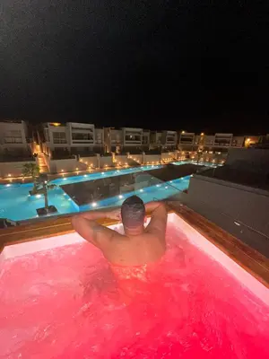 a man laying in a hot tub in a swimming pool at night at Lovely 1 Bedroom with private heated Jacuzzi at Sholan El Gouna in Hurghada