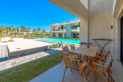 a patio with a table and chairs and a swimming pool at Cozy 2-Bedroom Apartment in G-Cribs, El Gouna. Terrace & Pool in Hurghada