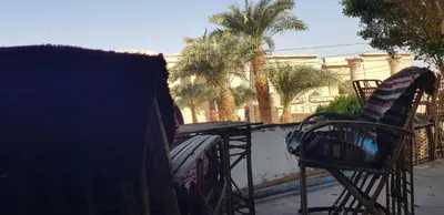 two chairs and a table on a balcony with palm trees at HabuHeritageHomeStayInLuxor in Al Aqālitah