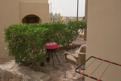 a patio with a grill and a chair and bushes at Private 1 bedroom flat with garden in Makadi in Hurghada