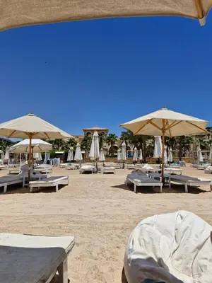 a beach with tables and umbrellas on the sand at Tawaya sahl hashesh in Hurghada