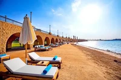 a beach with lounge chairs and an umbrella at AJIRA Resort Sahl Hasheesh in Hurghada