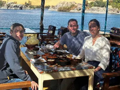 a group of three people sitting at a table with food at Nile View Guest House in Aswan