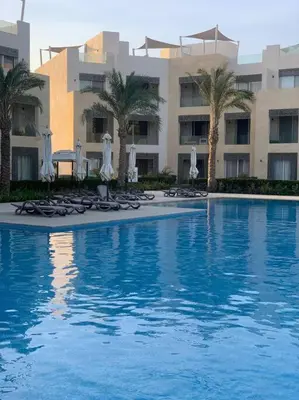 a swimming pool with chairs and umbrellas and a building at Mangroovy - 1BR Ravishing Lake and Mountain View in Hurghada