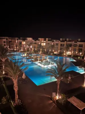 a large pool with palm trees and buildings at night at Mangroovy - 1BR Ravishing Lake and Mountain View in Hurghada