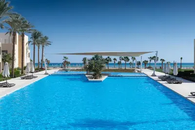 a swimming pool with palm trees and the ocean at Panoramic & Cushy 3BDR Mangroovy Free pool & Beach Access in Hurghada