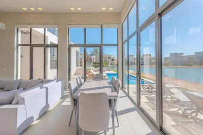 a living room with a table and chairs and glass windows at Ascot Bay, Premium 5BR Lagoon Beach House & Pool in Tawila, El Gouna in Hurghada