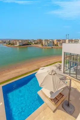 an umbrella and chairs next to a swimming pool at Ascot Bay, Premium 5BR Lagoon Beach House & Pool in Tawila, El Gouna in Hurghada