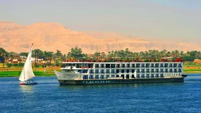 a large cruise ship on the water with a sailboat at Five-star Nile cruise 4 Night from Luxor to Aswan every Monday, Thursday and Saturday in Aswan
