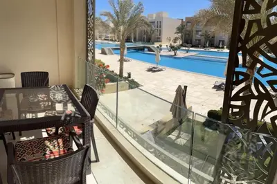 a balcony with a table and chairs and a swimming pool at Mangroovy Comfy 2 Bedroom in Hurghada