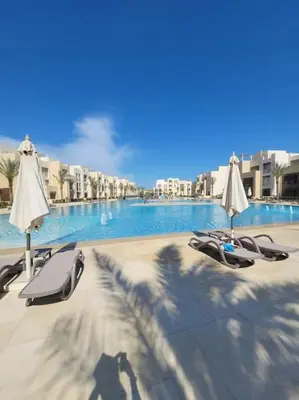 a beach with chairs and umbrellas next to a pool at Mangroovy Comfy 2 Bedroom in Hurghada