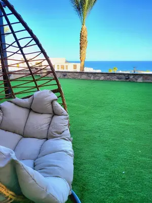 a couch sitting on the grass next to the beach at Apartment Azzura Sahl Hasheesh with private garden in Hurghada