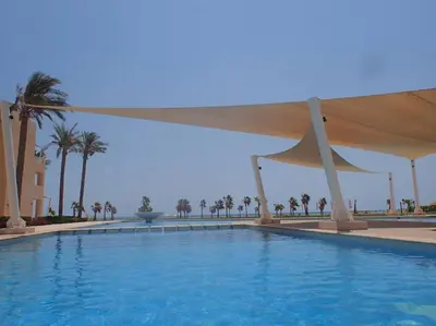 a large blue swimming pool with a white umbrella at Mangroovy 1br Charming Escape Hilton pool view in Hurghada
